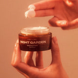 one hand holding a jar of plant apothecary night garden while another hand dips fingers into night cream